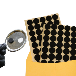 Black filter patches on yellow envelope with jar lid held by a gloved hand